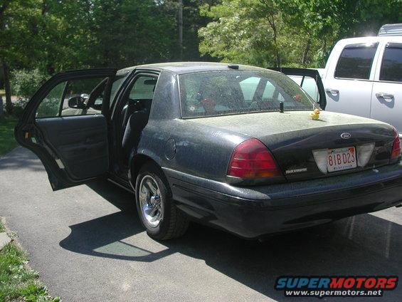 Dark Ford Crown Victoria with rear doors open, parked next to a white pickup truck