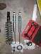 2002 Toyota Sequoia - A collection of new and old shock absorbers, along with a spring compressor tool, are laid out on a concrete floor.
