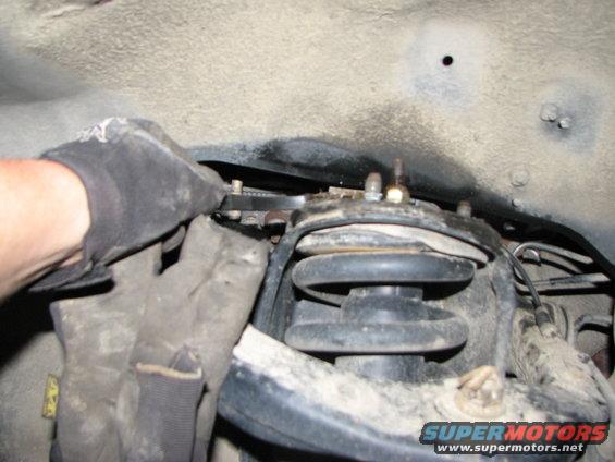 Suspension part with gloved hand using wrench. SuperMotors.net logo visible