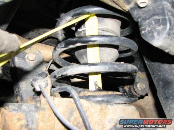 Suspension spring with yellow measuring tape wrapped around it. Some text is visible on the tape