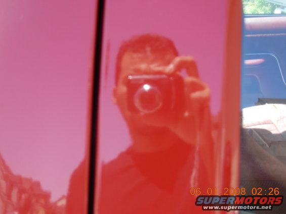 Reflection of person holding camera in shiny red truck door