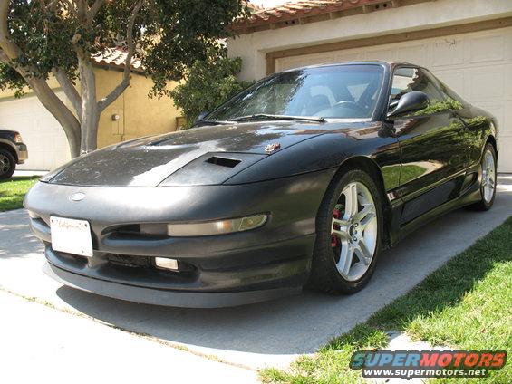 Black sports coupe parked in driveway, front quarter view. Hood has two vents