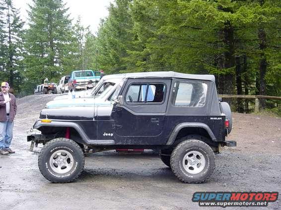 Side view of a black Jeep Wrangler with a man standing nearby. Other vehicles are in the background