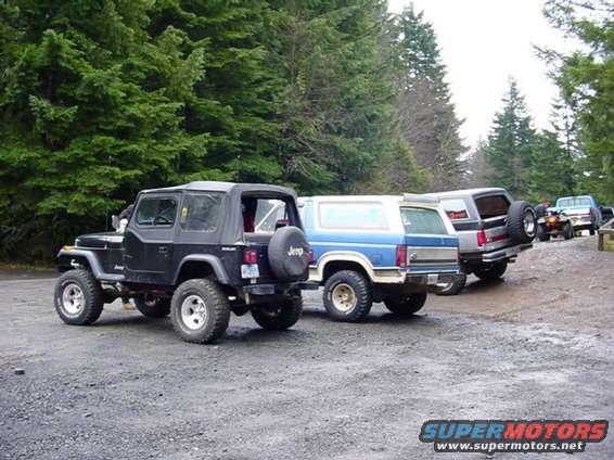 1995 Jeep Wrangler parked next to a blue SUV and a silver SUV, with trees in the background