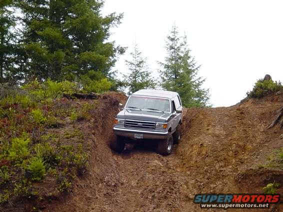 Gray Ford Bronco climbing a muddy hill, front 3/4 view