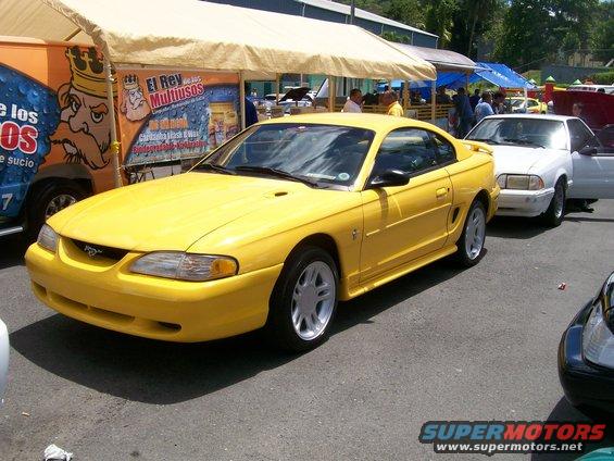 Yellow Ford Mustang parked next to a white car under a tent