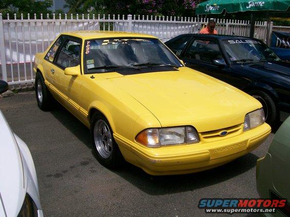 Yellow Ford Mustang coupe, front 3/4 view. Visible text 'Mustang' on bumper