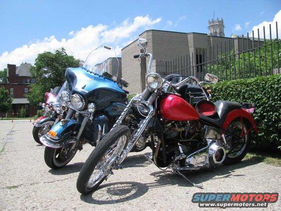 Two motorcycles parked side-by-side, one red and one blue, with a building and trees in the background
