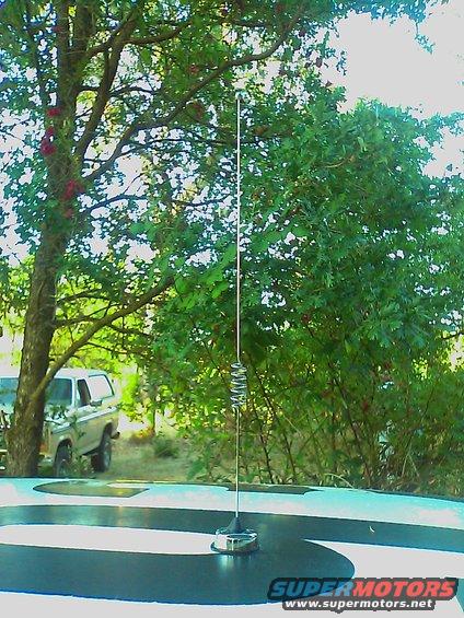 Car antenna on a roof with a tree and an old pickup truck in the background