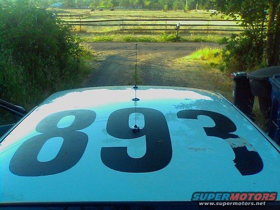 Car roof with numbers 893 painted on it, antenna in middle. Rural background with fence and trees