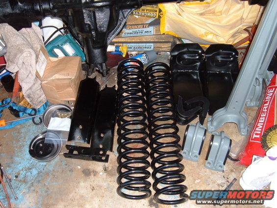 Vehicle suspension parts laid out on a floor, including springs, shocks, and a differential housing