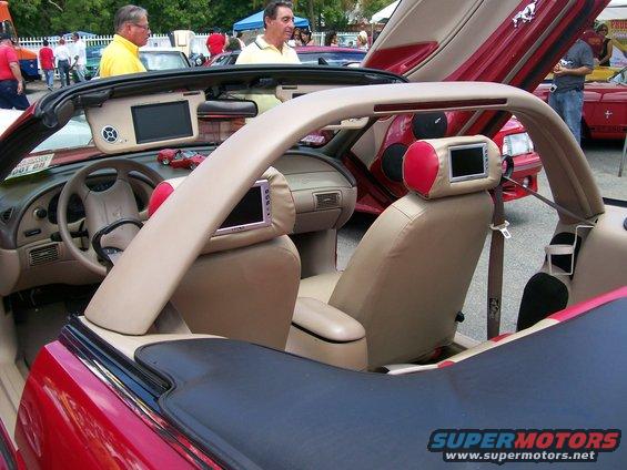 Interior of a red 2001 Ford Mustang convertible with screens on headrests and doors open