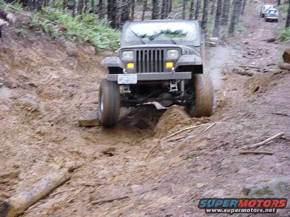 Gray Jeep Wrangler driving through mud on a wooded trail