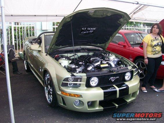 Light green convertible Ford Mustang with black racing stripes, hood open revealing engine, chrome rims