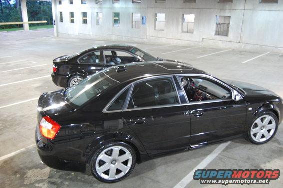 Two black sedans parked in a lot. One is in the foreground, the other is behind it