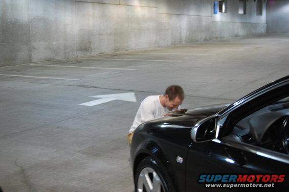 Black 2002 BMW M3 with a man bending over the hood in a concrete parking garage