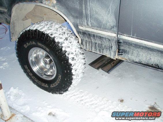 Side view of a vehicle's fender and Mickey Thompson Baja MTZ tire covered in snow