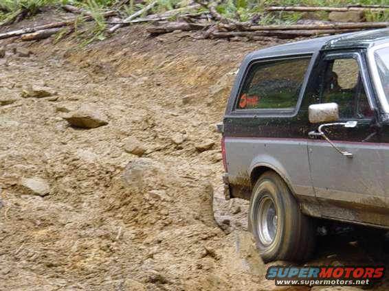 Side view of a black and gray Ford Bronco II driving on a muddy, rocky trail