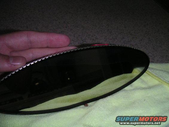 Close-up of a dark rear view mirror with a metal retaining clip edge, held by a hand