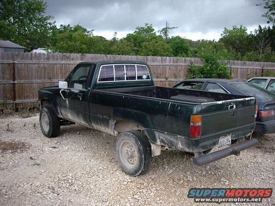 dark green pickup truck parked next to a fence, with another car behind it