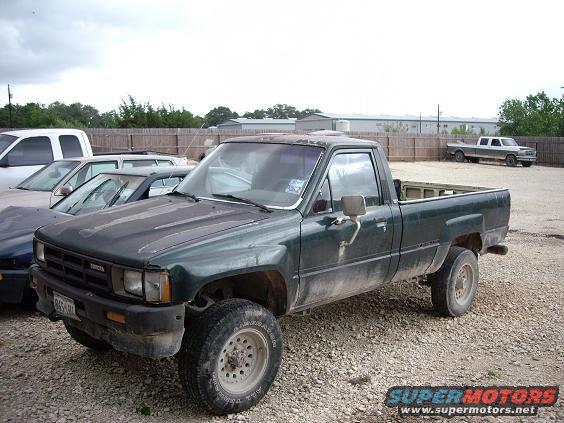 Green Toyota pickup truck, front quarter view, dusty, with worn hood and aftermarket wheels