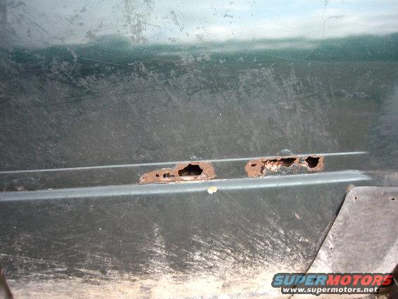 Rust holes on lower door panel of a green vehicle