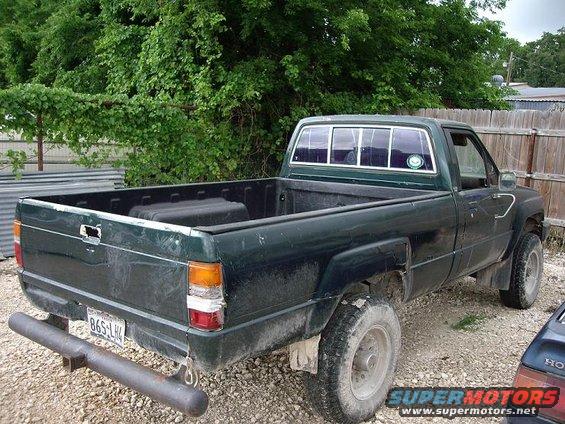 Rear view of a dark green pickup truck with a custom bumper and a partial view of another vehicle on the right