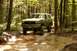 1987 Ford Bronco - A 1987 Ford Bronco navigates a water-filled path in a dense forest.