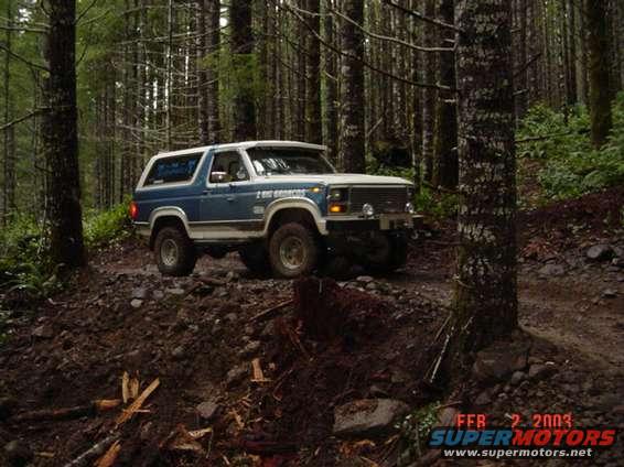 Blue and white SUV on a forest trail. Text on door reads '2 BIG BRONCOS'