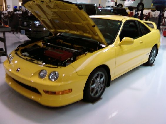 Yellow coupe with hood open, showing red engine cover. Front 3/4 view