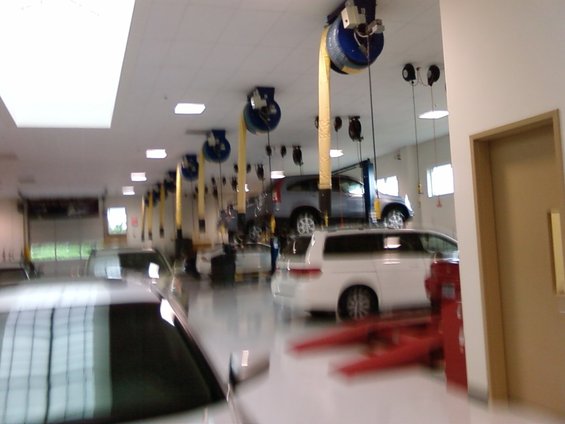 Car repair shop interior with vehicles on lifts and floor, overhead equipment, and doors