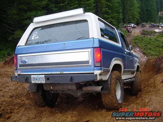 Blue and white Ford Bronco on a muddy trail, rear view. License plate UKW 650