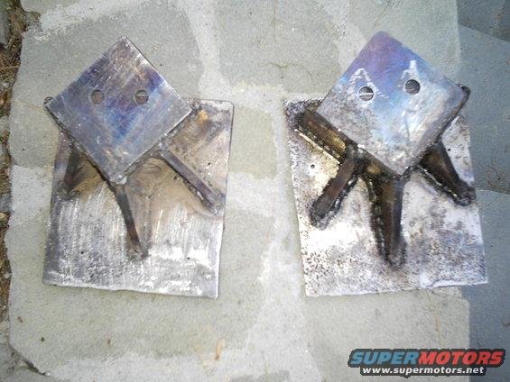 Two welded metal shackle flip brackets on a stone surface