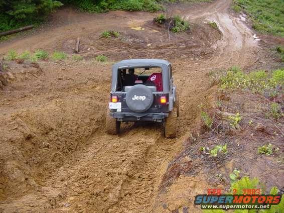 Jeep Wrangler driving up a steep, muddy path. Spare tire on the back has 'Jeep' logo