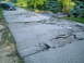 2001 Dodge 2500 - A black van is parked on a road that has sustained significant damage, with large cracks and sections of pavement collapsed.