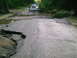 2001 Dodge 2500 - A silver van drives over a severely damaged road and bridge, likely due to flooding.