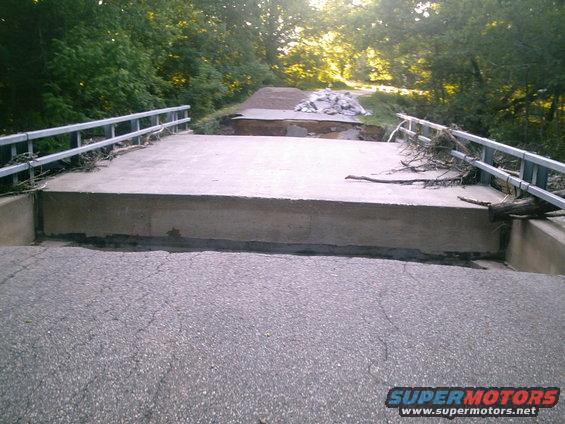 Damaged bridge over a creek with debris and trees on the side