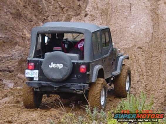1995 Jeep Wrangler with soft top on a dirt trail, rear view. Spare tire mounted on the back
