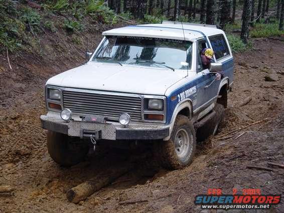 White and blue Ford Bronco II driving through mud on a trail