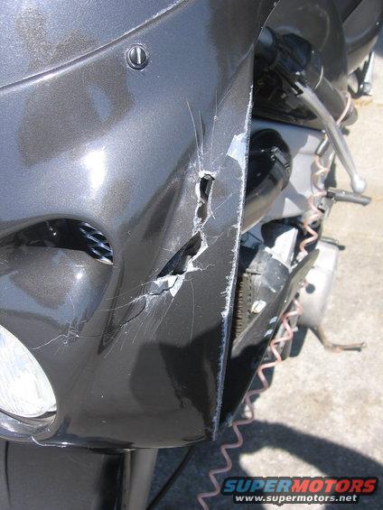 Close-up of a cracked and scratched dark gray motorcycle fairing with visible damage