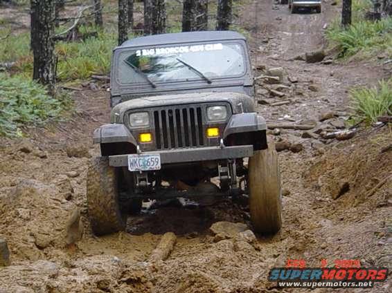Dark gray Jeep Wrangler driving on a muddy, rocky trail. License plate WKC 659