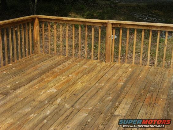 Wooden deck with wooden railing. A metal object is visible in the background