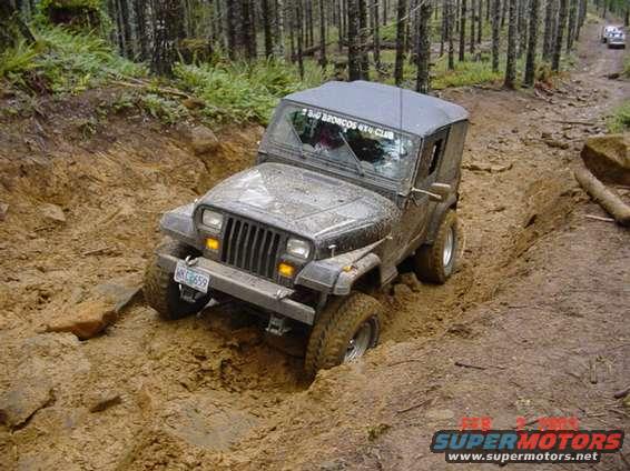 1995 Jeep Wrangler stuck in a muddy rut on a forest trail, with a sticker on the windshield reading 'BIG BRONCOS 4X4 CLUB'