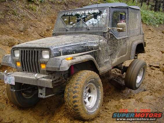 Mud-covered Jeep Wrangler on a dirt trail, with a sticker on the windshield reading 'BIG BRONCOS 4X4 CLUB'