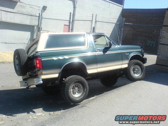 Green and tan Ford Bronco with a spare tire on the back, angled on a curb