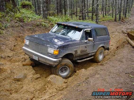 Dark blue 1990 Ford Bronco stuck in mud on a wooded trail