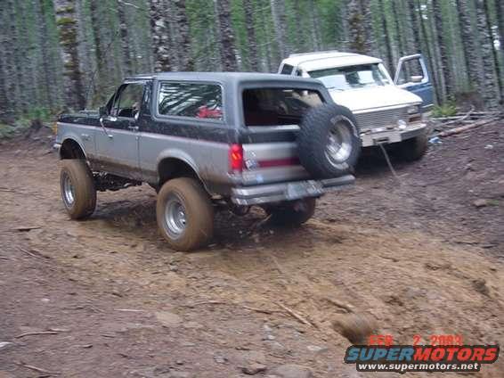Silver and black SUV with spare tire on rear, parked on dirt path with white SUV behind