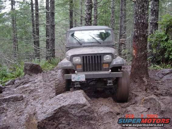 Jeep Wrangler navigating a steep, muddy, rocky trail in a forest. License plate reads WYO 659