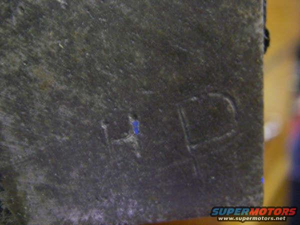 Close-up of a dark, textured engine block casting with faint stamped letters 'HP' and a blue mark