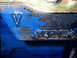1968 Ford Mustang - Close-up of an engine block reveals partial casting numbers and a stamped 'V' symbol under chipped blue paint.
